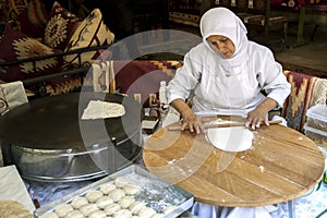 A lady rolls Turkish flat bread before placing it onto a hot plate cooker.