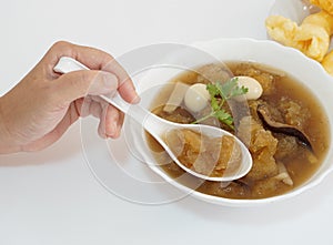 Lady's hand using a spoon to scoop Chinese style soup or braised fish maw in red gravy