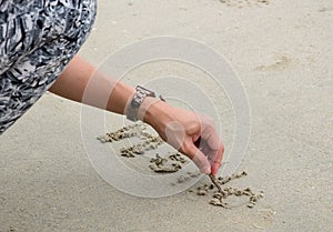 A lady`s hand writing word `HELLO` on the sand at the beach