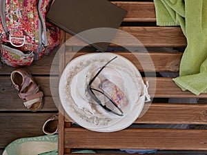 A lady`s summer hat, sunglasses, a book and a light green cotton towel lie on a wooden sunbed on a Sunny summer day on the beach w