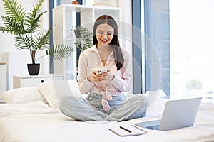 Lady sitting on bed and enjoying chatting with coworkers using smartphone.