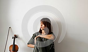 Lady sitting on ground floor,against on the wall,beside violin and bow