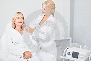 Lady in sitting and professional cosmetologist cleaning with dermabrasion tool photo