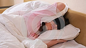 Lady in sleeping mask lies in bed closing ear with pillow