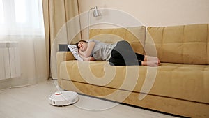 Lady sleeps on sofa while robot cleaner hoovers in room