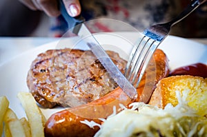 Lady slice sausage and pork steak on white dish photo