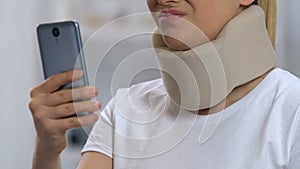 Lady with smartphone in foam cervical collar feeling neck pain, rehabilitation