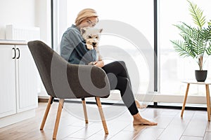 Lady snuggling white furry dog in kitchen on sunny day