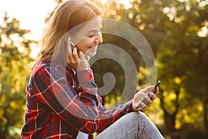 Lady student sitting in the park using mobile phone listening music.