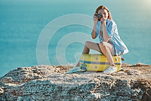 Lady take picture on photocamera sitting on bright yellow suitcase. Business travel and new ground concept, copy space