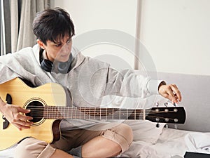 Lady is tuning the wooden acoustic guitar strings by by listening the note sounds through headphones