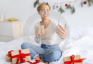 Lady using cellphone making videocall on Xmas holding present