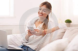 Lady Using Cellpone And Laptop Relaxing On Couch At Home