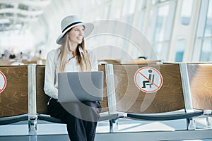 A lady is using her laptop while expecting her flight. Tourist freelancer works and waits for flight in waiting room