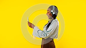 Lady Using Smartphone Wearing Headphones Over Yellow Background, Side View