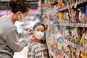 A lady  wearing a protective mask puts a face mask on a daughter in  supermarket. Safety during COVID-19 outbreak. Epidemic of