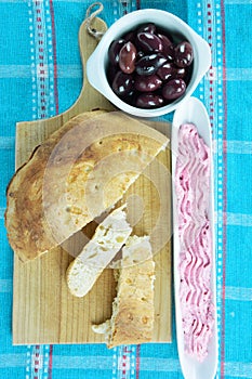 Lagana bread on cutting board, taramosalata on olive dish and kalamon olives on bowl