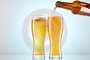 Lager, ale flows to empty tall glasses from bottle.