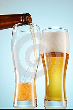 Lager, ale flows to empty tall glasses from bottle.