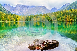 Laghi di Fusine inferior lake, Tarvisio, Italy. Autumn landscape with water, forest and Mangart mountain, nature travel background