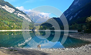 Lago di Tenno with its clear water in the morning light. Two people standing on the bank. Trentino, Italy