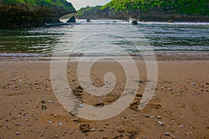 Lagoon bay surrounded from green rock hills. Foot prints in sand beach