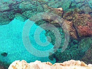 Lagre stones in the blue water. Rocky bottom of the sea with white sand. Top view from the cliff.