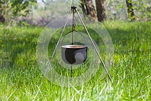 Lagre touristic cauldron on a tripod among forest glade with green grass