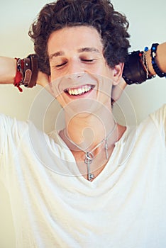 Laidback and stylish dude. Studio shot of a handsome young man laughing while holding his hands behind his head.