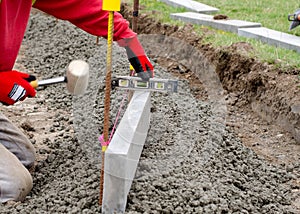 Laing edging kerb on semidry concrete during roadworks and new footpath construction by groundworker wearing safety gloves