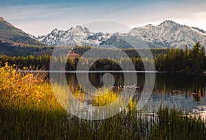 Lake in autumn scenery on sunrise with beautiful and snowy mountains on background. Strbske pleso in High Tatras in fall with