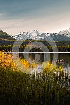 Lake in autumn scenery on sunrise with beautiful and snowy mountains on background. Strbske pleso in Tatras in fall with yellow