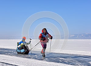 LAKE BAIKAL, IRKUTSK REGION, RUSSIA - March 08, 2017: Man on skates rolls girl on sledge drag