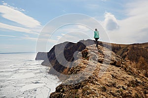 Lake Baikal in spring. White ice floes melt on the water. A woman stands on a rock and enjoys a beautiful view.