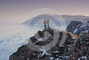 Lake Baikal in Winter. Couple Travelers Standing on Top of Mountain and Looking at Frozen Baikal lake, Russia
