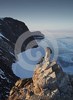 Lake Baikal in Winter. Woman Sitting on a Cliff and Looking on a Frozen Baikal lake. Olkhon Island, Russia