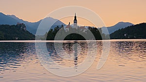 Lake Bled in Slovenia at sunrise. In the foreground, an island with the Assumption of Maria Church, and the Alps in the background