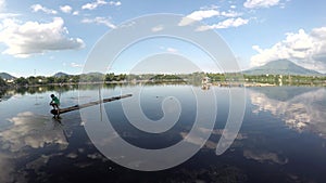 Lake boatman paddles his bamboo raft toward the shore of mountain lake