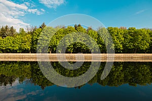 A lake in the city park early in the morning. Quiet and peaceful, in harmony, no people. Fresh green trees and grass, blue sky and