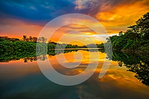 Lake in an dramatic sunset. Lake surrounded by trees at sunset with orange sky and clouds in bluish gray tones forming a beautiful