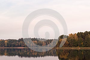 Lake and far shore at fall time. Faded colors and calm water grey sky main scene