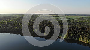 Lake, forest and yellow field in spring sunrise light 4k aerial top view. Fly above water of lake Dolgoe, Belarus.