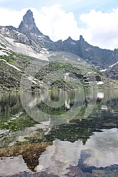 Lake Gornykh dukhov surrounded by tall mountain peaks covered in snow. Water reflecting mountains and sky. Ergaki park