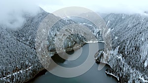 Lake in the mountains surrounded by forest in winter season. Flying above