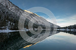 Lake plansee at winter sunrise with mirroring alpine mountain