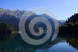 Lake Ritsa surrounded with high caucasus mountains mirroring in water