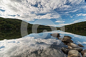 Lake with rocks in the foreground and reflection of sky and surrounding forest photo