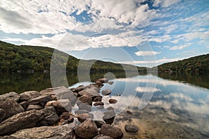 Lake with rocks in the foreground and reflection of sky and surrounding forest photo