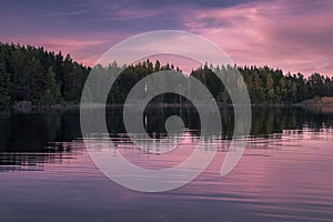 Lake in Scandinavia during sunset / sunrise with beautiful violet lights from the sun and some forest silhouette