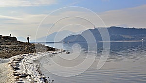 Lake shore with a strip of snow and standing person on the stone